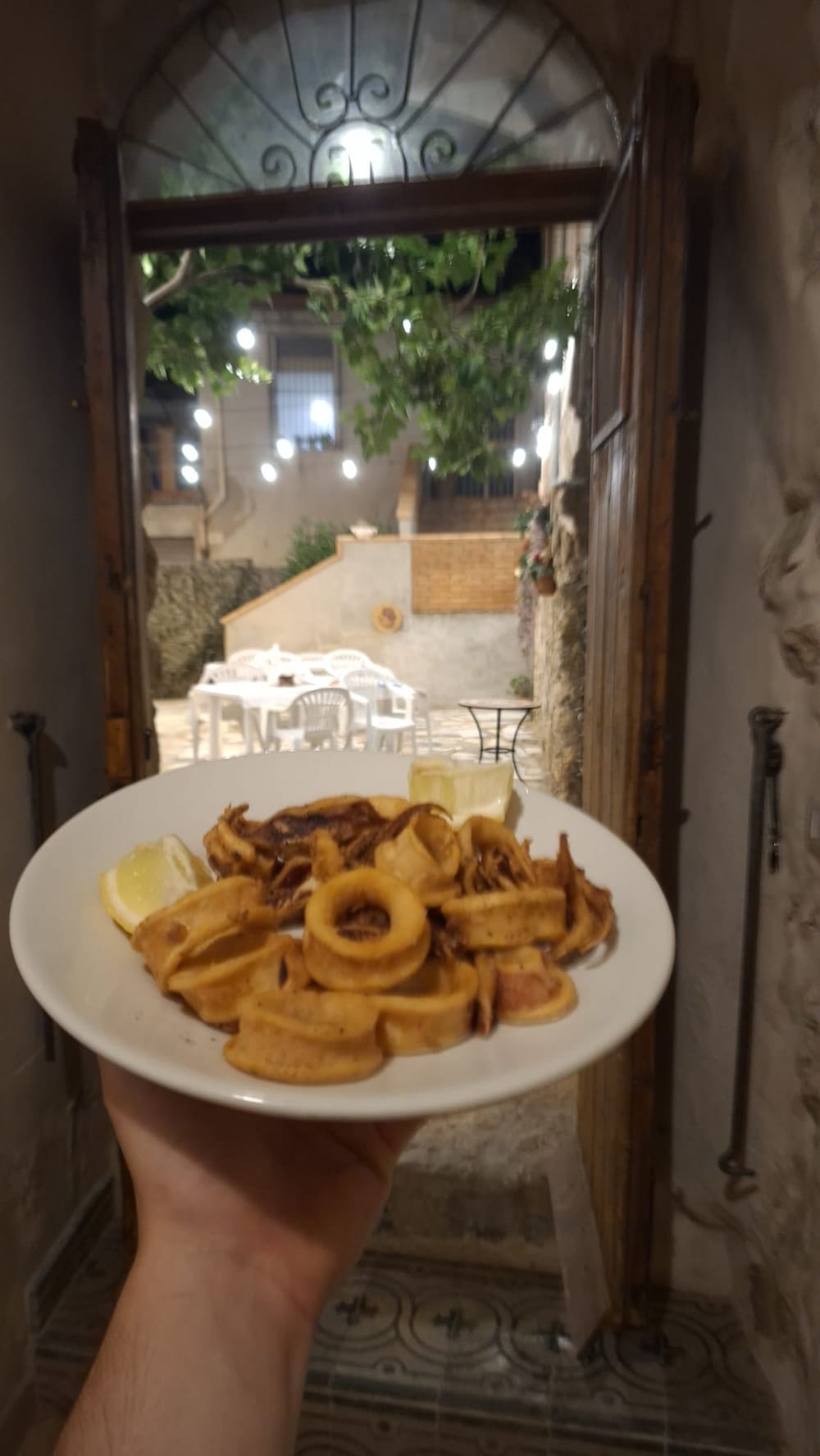 Un piatto di calamari fritti con limone, servito sulla soglia della porta che si apre sul cortile illuminato